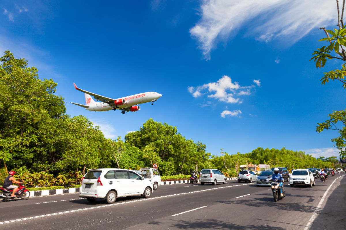 Airplane coming into land at Bali Airport flies over cars on road in daytime.jpg