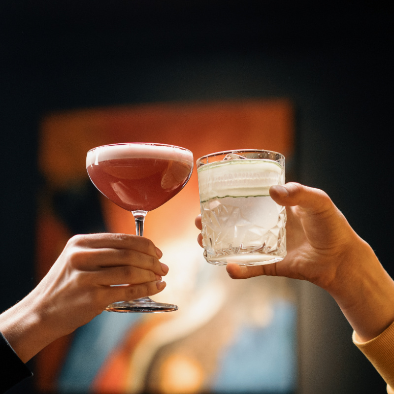 Two-People-Cheers-Cocktails-At-Bar