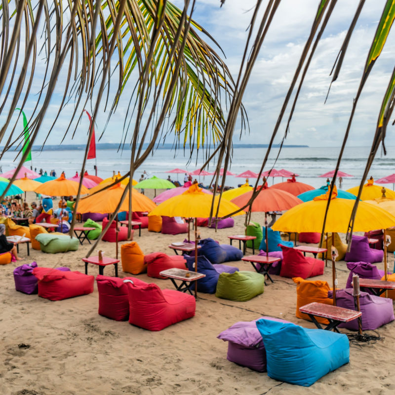 Colourful-Beanbags-on-Seminyak-Beach-Under-Palm-Leaves-on-Bali-Beach