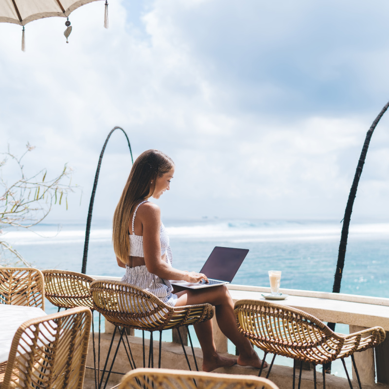 Digital-nomad-woman-works-at-high-table-desk-overlooking-ocean-in-Nusa-Penida