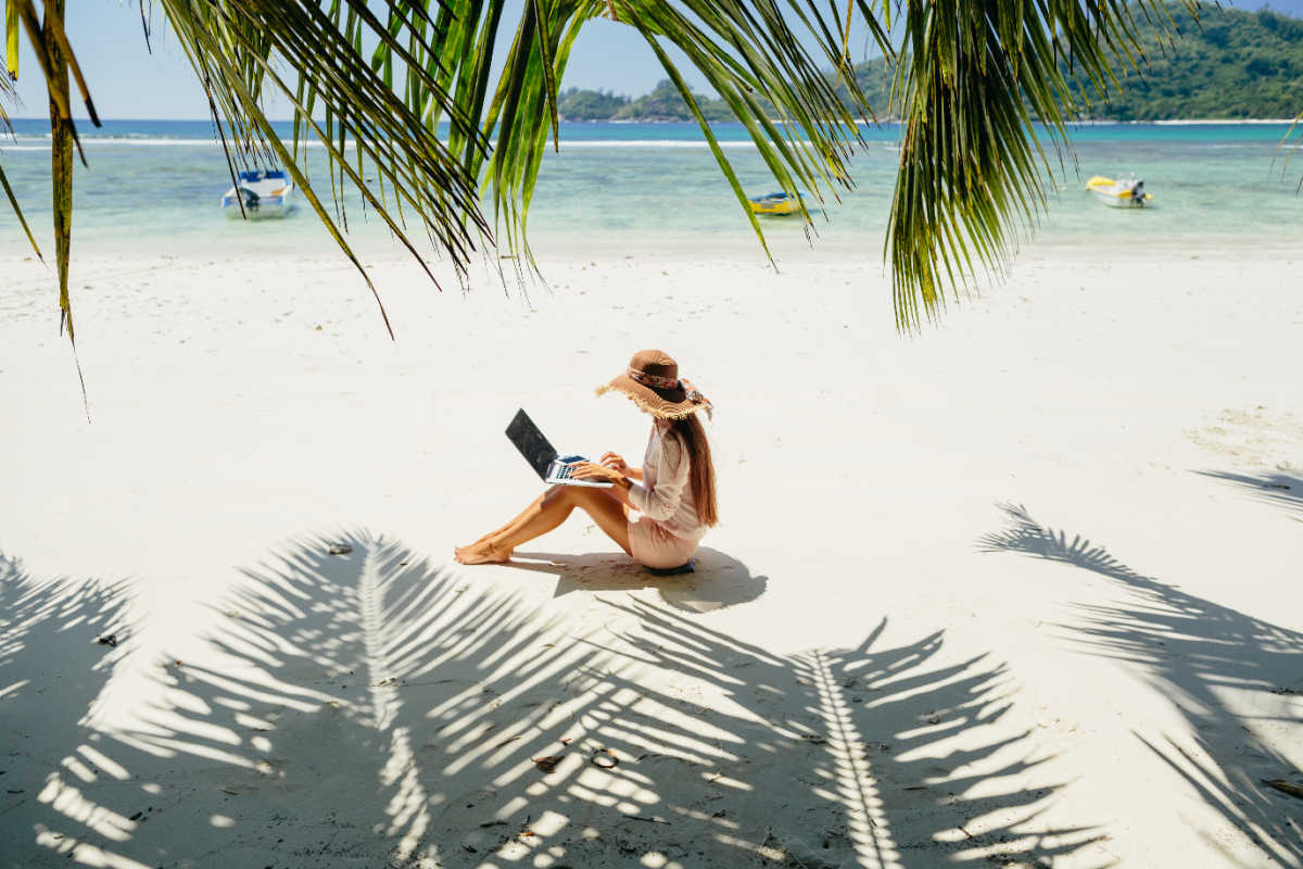 Woman works on laptop on beach beneath palm trees.jpg