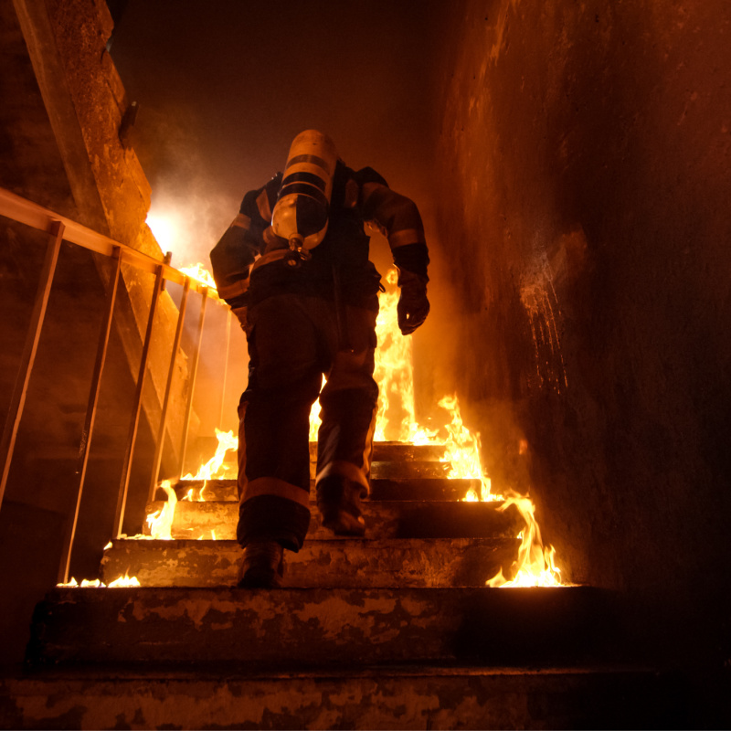 Petugas pemadam kebakaran menaiki tangga di gedung yang terbakar.jpg