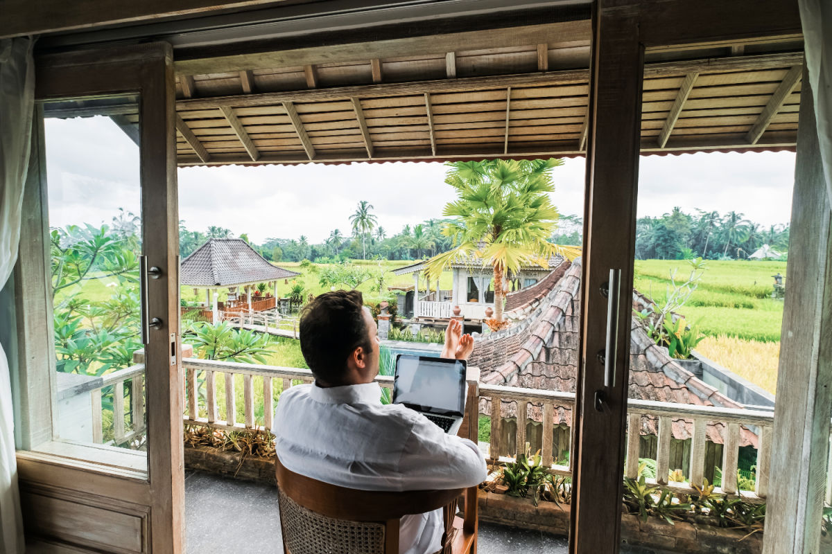 Male digital nomad sitting with laptop on the balcony of his villa in Bali