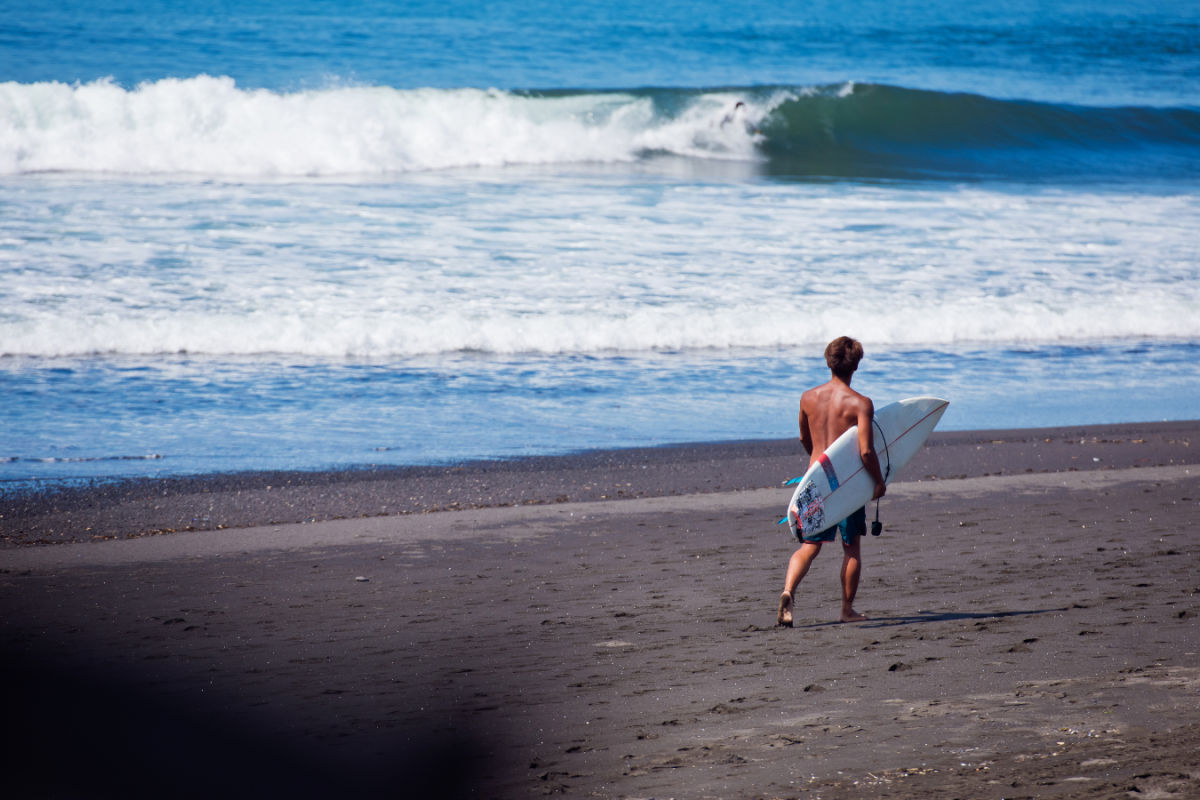 Surfer Walks Along Black Sand Bali Beach Keramas.jpg