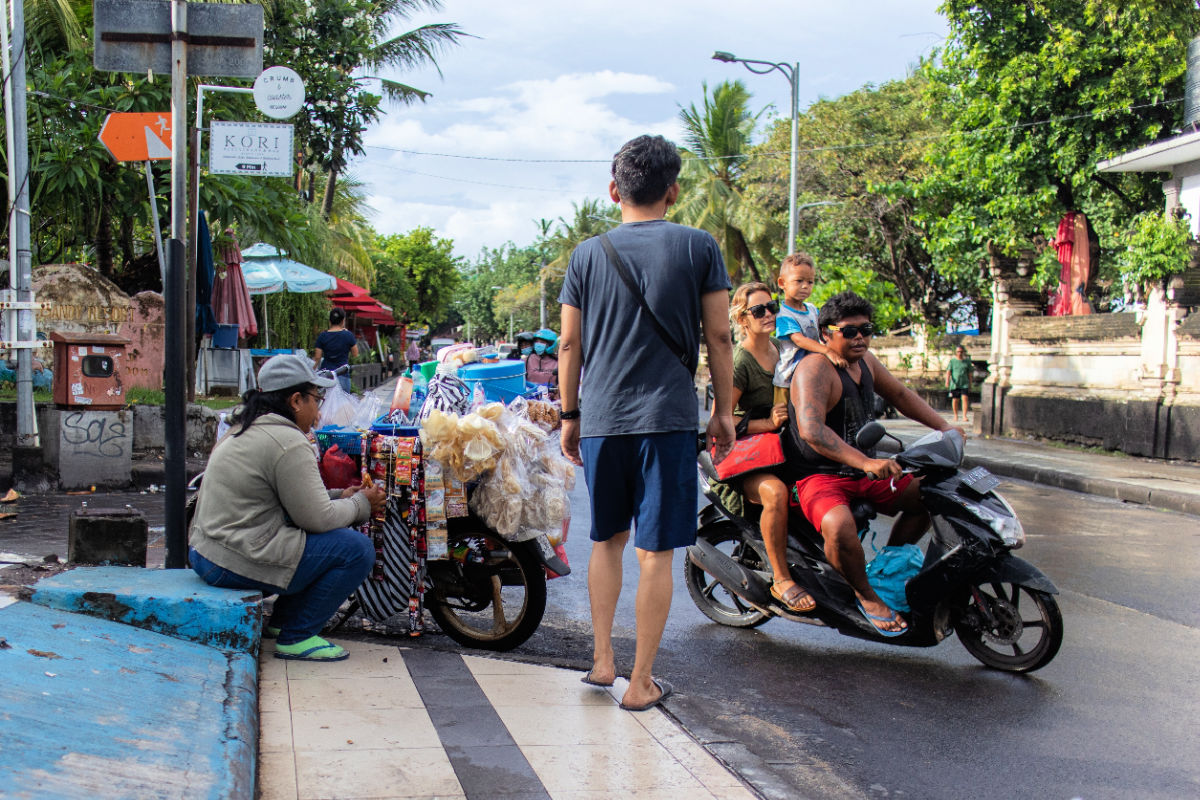 Scene on Bali Street Tourist Walks Family Drives Woman Sells Snacks.jpg