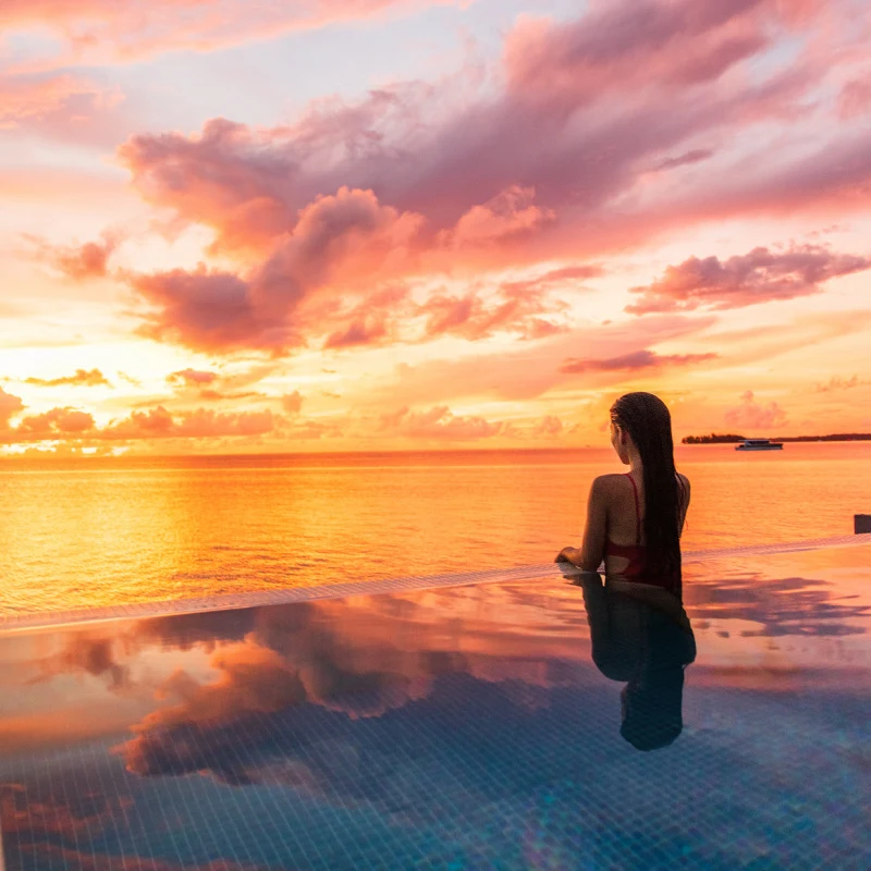 Woman in Ocean Facing Infinity Pool at Sunset