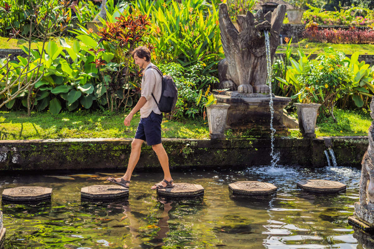 Man Walks Over Stepping Stones At Tirta Gangga East Bali.jpg