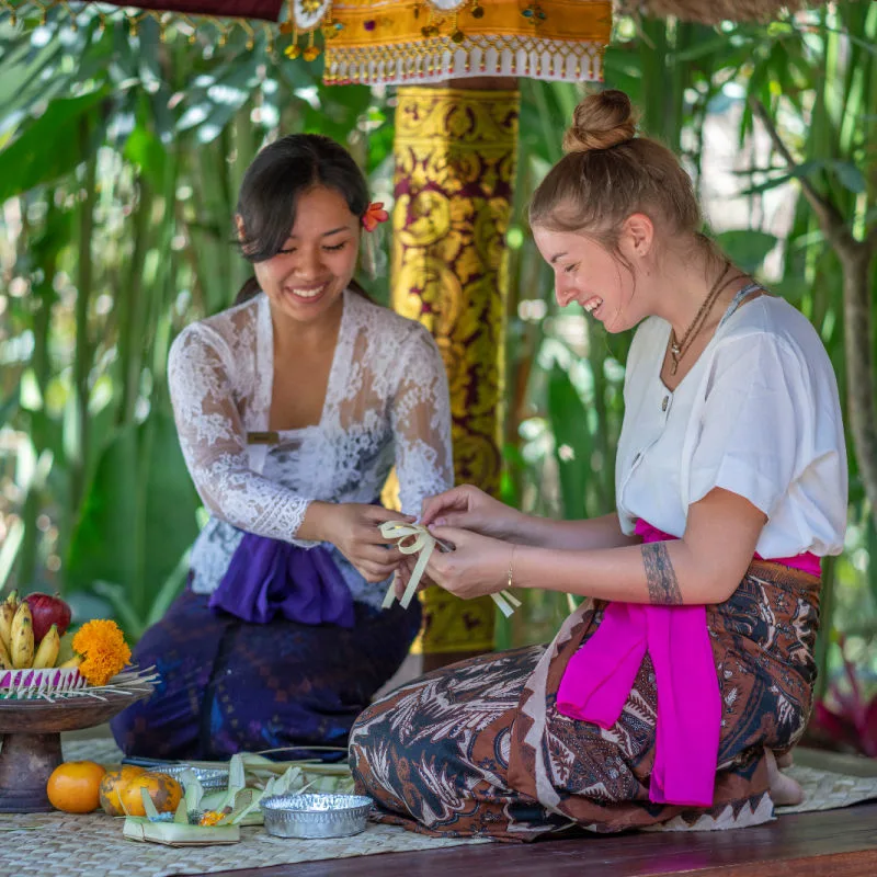 Balinese Woman and Tourist Make Canang Sari.jpg