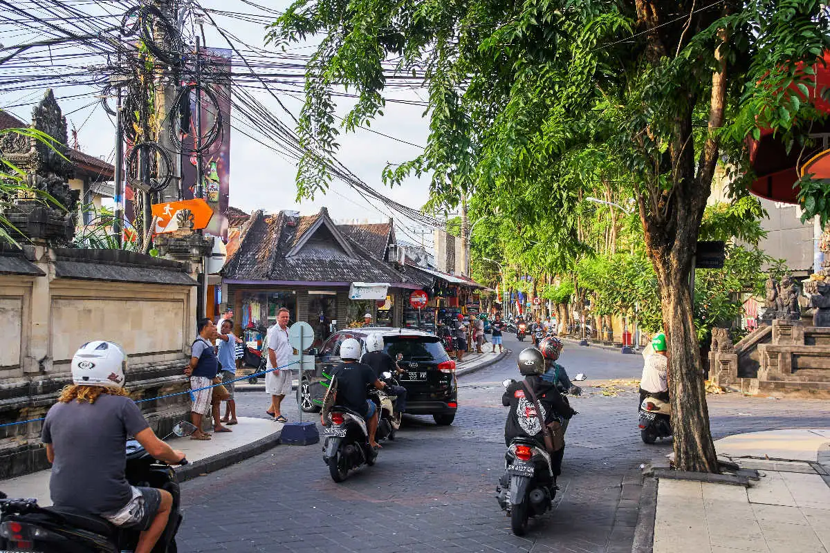 Tourists and locals drive mopeds and cars on Bali road