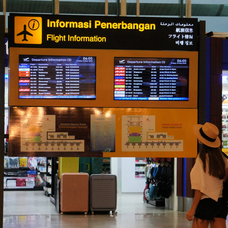 Airport Passenger Looks At Flight Board in Bali Airport